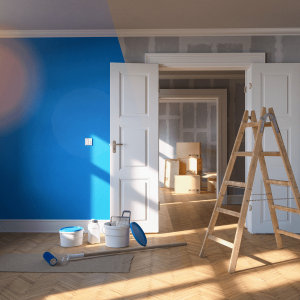 This image showcases an interior wall painting project in progress. The scene depicts a room with one wall partially painted in a bright, bold color. A paint roller attached to a long handle is seen mid-stroke, applying a swath of vibrant paint to the wall. A paint tray filled with the same color is visible on the floor below, with a drop cloth spread beneath it to protect the flooring from potential drips and spills. The room appears to be well-lit and features hardwood flooring. The other walls and ceiling in the room are painted in a light, neutral color, which provides a stark contrast to the wall being painted. In summary, the image captures a moment in the process of transforming a room through the application of bold, colorful paint to an interior wall.